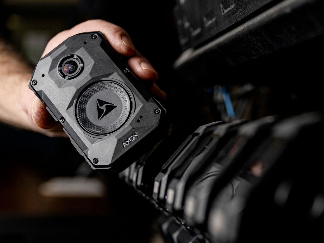 An Axon Body 4 camera lifted from its dock, with the other cameras in the dock behind it.