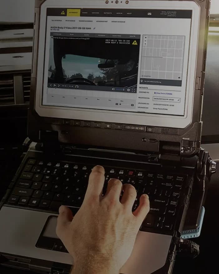 A rugged in-car laptop showing the video and map screen of the Axon Evidence platform