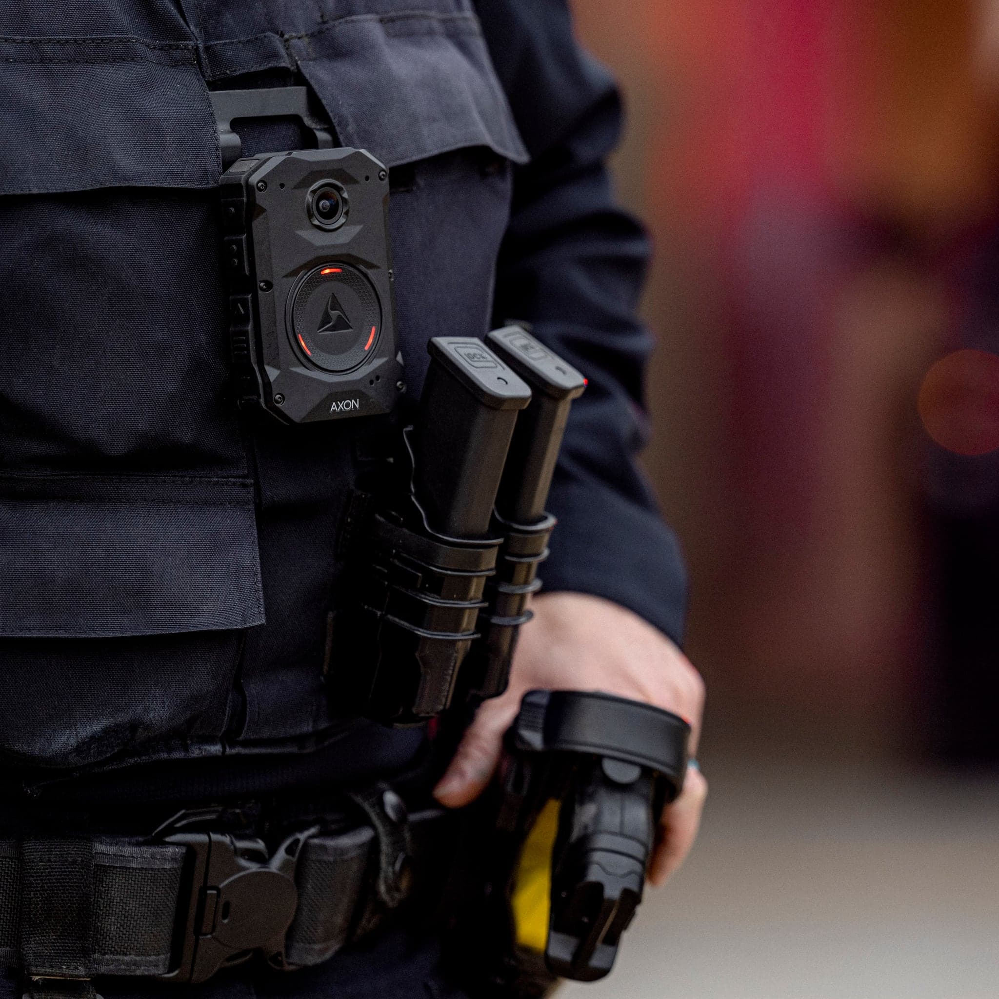 An officer wearing an Axon Body 4 camera on the chest, a hand resting on a holstered TASER 10 energy weapon.