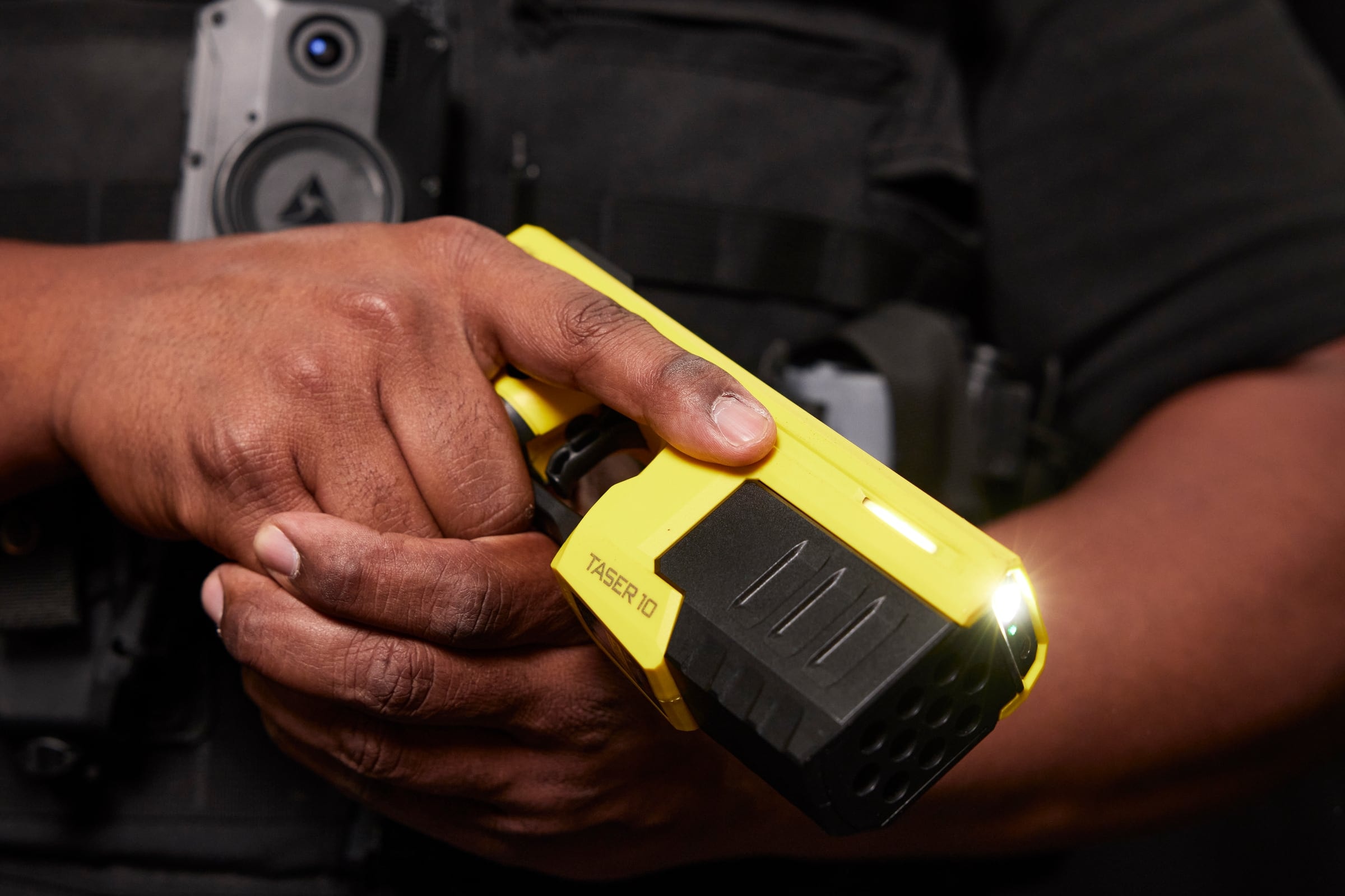 The TASER 10 energy weapon in an officer's hands, with an Axon body-worn camera on the chest.