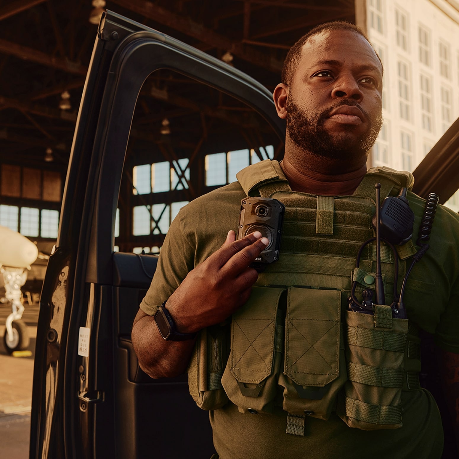 A security officer in an aircraft hangar, with an Axon Body 4 camera on the chest.