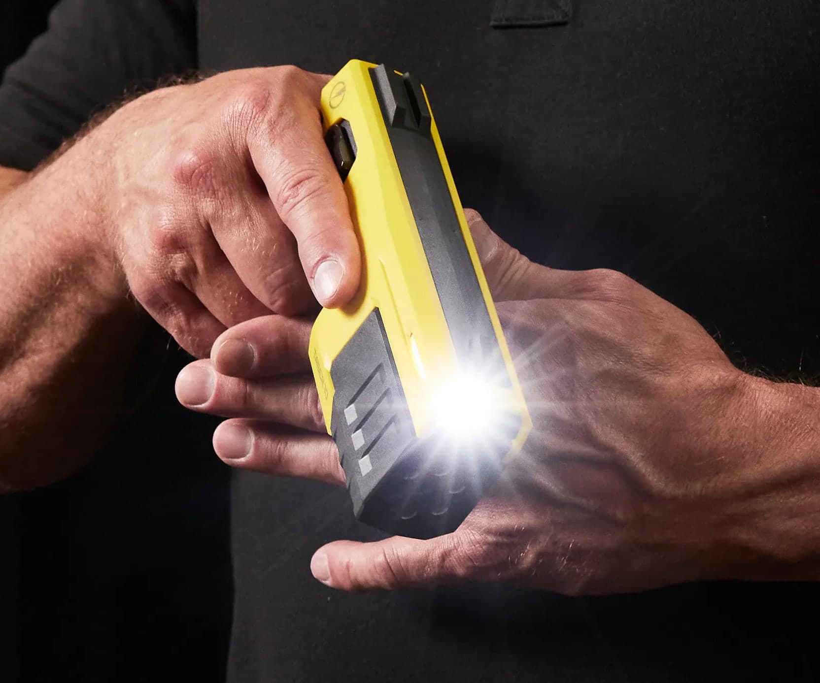 The TASER 10 energy weapon in two hands, its light on, against black.