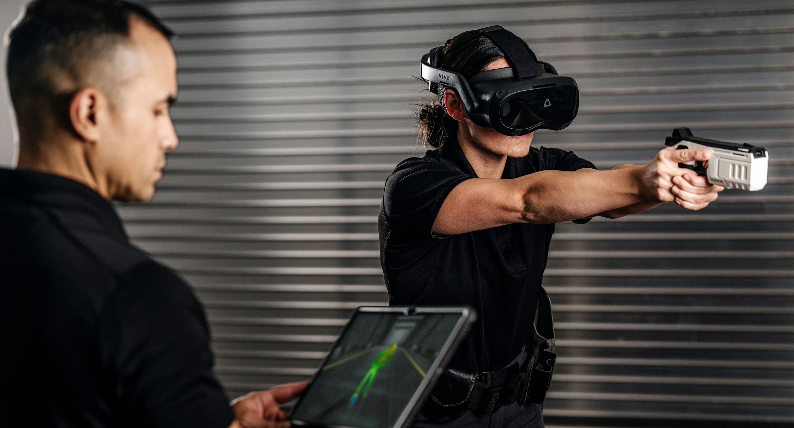 Training with the Axon VR training system: a trainee in a VR headset points a TASER 10 VR training controller into a virtual scenario while an instructor follows on a tablet.
